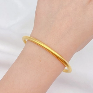 Bracciale rigido minimalista in oro opaco per donna su uno sfondo bianco strutturato