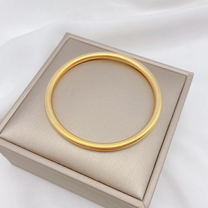 Dettaglio di un bracciale in oro opaco su cuscino di seta con trama fine sabbiata