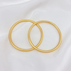 Dettaglio di un paio di bracciali rigidi in oro opaco minimalisti con design tondo