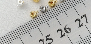 Makroaufnahme von 14K goldgefüllten Crimp-Perlen für Schmuckherstellung neben einem Lineal