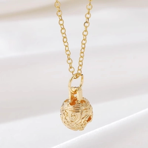 Macro view of 14K gold hollow spherical bell pendant with detailed floral engraving