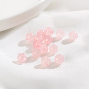 Makro-Detail von rosa Achatperlen auf weißem Stoff für DIY-Schmuckherstellung