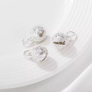 Three hollow silver tiger head bell pendants for DIY jewelry making on white ceramic tray