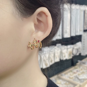 Close-up of 18k gold leaf-shaped earring with colorful crystal stones on woman's ear