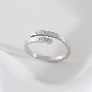Bague ajustable en acier inoxydable gravée Trust God sur un fond blanc minimaliste