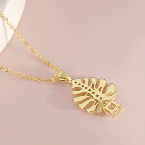 Elegante collana a foglia di monstera in oro 18 carati con zirconi su sfondo rosa