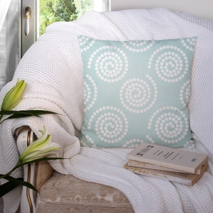 Mint green square pillow cover with white spiral geometric patterns on a cozy armchair
