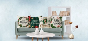 Close-up of four festive Christmas pillow covers with reindeer and wreath on green sofa