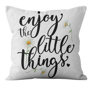 Detail view of white cushion cover featuring enjoy the little things text and daisies