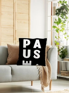 Detail view of square black linen pillow cover featuring bold white PAUSE text on a grey sofa