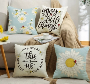 Set of four daisy pillow covers with floral patterns and quotes on a cozy grey sofa