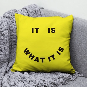 Bright yellow square throw pillow with It Is What It Is print on grey sofa background