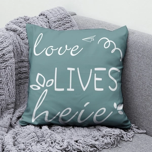 Detail view of teal pillow with white Love Lives Here text on a grey sofa