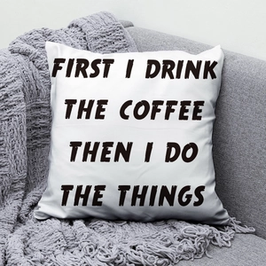 Detail of white square peach skin pillow with coffee quote resting on a grey sofa