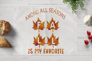 Detail of linen placemat with orange maple leaf print and Fall typography on wood