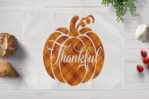 Detailed view of white linen placemat with plaid pumpkin and Thankful text for autumn decor