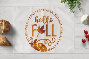 Detail of hello FALL themed placemat with pumpkins and maple leaves on a white wood table