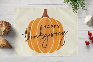 Top-down view of Thanksgiving pumpkin placemat on a white wooden table with decor