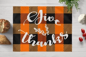 Detail of harvest buffalo plaid placemat with Give Thanks print on white wood surface