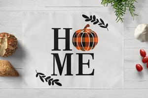 Detail of linen placemat featuring HOME pumpkin print on a white wood surface