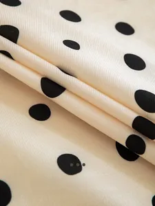Macro shot of smooth cream fabric with black polka dots and fine twill weave texture