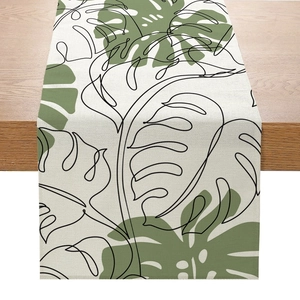 Détail d'un chemin de table en lin avec feuilles de monstera sur table en bois clair