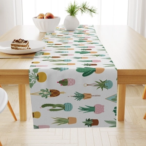 Detail of linen table runner featuring hand-drawn cactus patterns on a wooden dining table
