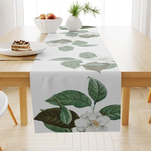 Linen table runner with white camellia and leaf pattern on a wooden dining table