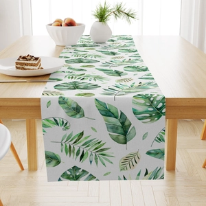Close-up of a linen table runner featuring tropical green leaf patterns on a wooden table