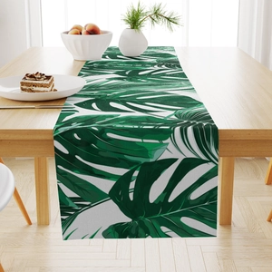 Linen table runner detail with green monstera leaves on a light wood dining table