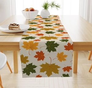 Detail view of linen table runner featuring vibrant autumn maple leaf prints on a wooden table