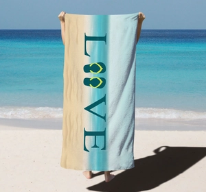 Detail of microfiber beach towel featuring LOVE letters and flip-flops on a sandy beach
