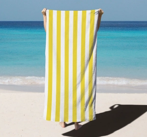 Vertical yellow and white striped microfiber beach towel held open on a sunny coast scenery