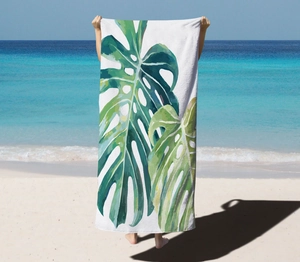 Detail of microfiber beach towel featuring vibrant green tropical monstera leaf print