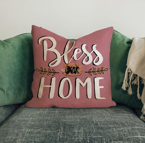 Detail of dusty pink linen pillow cover with Bless OUR HOME text on a grey sofa