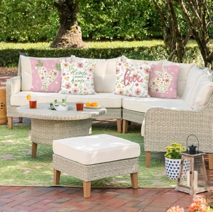 Detail of four floral Easter pillow covers with pink rabbits on an outdoor rattan sofa