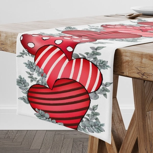 White table runner with red hearts and green leaves on a solid wood dining table