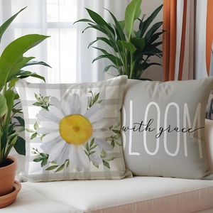 Close-up of linen cushion covers with white daisy print and bloom with grace slogan