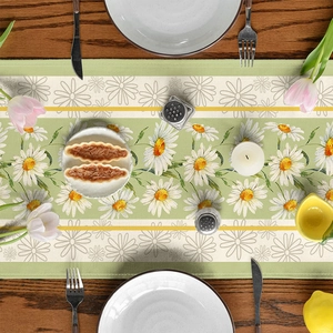 Detail of a floral table runner with white daisies on a wooden table with tableware