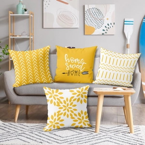 Set of four modern yellow and white decorative pillow covers on a grey sofa