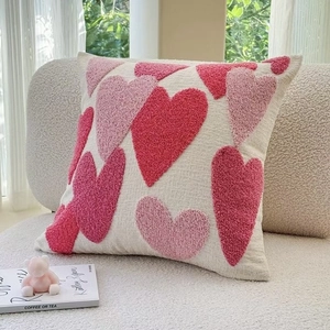 Square embroidered heart pillow cover with tufted texture on a cream sofa