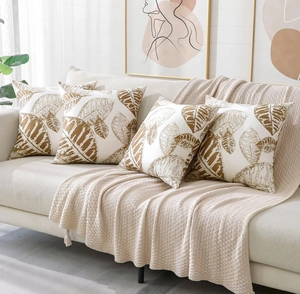 Set of four peach skin pillow covers with brown botanical leaf patterns on a sofa