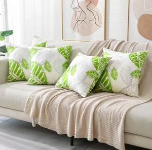 Set of 4 white pillow covers with green leaf patterns displayed on a beige sofa