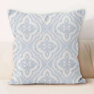 Detail of white throw pillowcase with light blue symmetric geometric patterns on a sofa