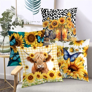 Set mit vier Kissenbezügen mit Hochlandrind- und Sonnenblumenprint auf einem Sofa