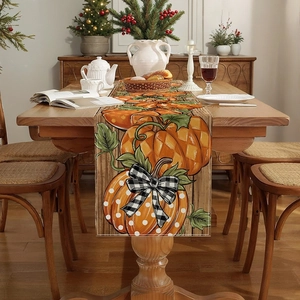 Detailed view of autumn pumpkin table runner with buffalo check bows and green leaves