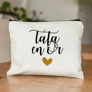 Detail of white canvas pouch with Tata en Or text and golden heart on wooden table