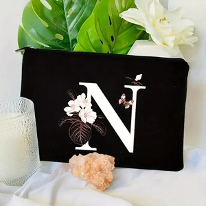 Detail of black floral letter N makeup bag on white fabric with aromatic candle and leaves