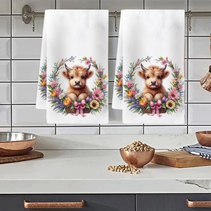 Detail of hanging kitchen towels featuring highland cow and floral print on white tiles
