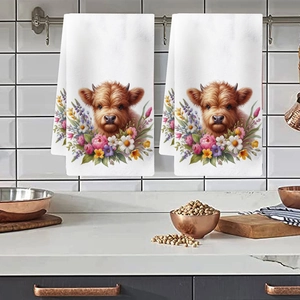 Detail view of white kitchen towels featuring highland cow and floral print hanging on a rack